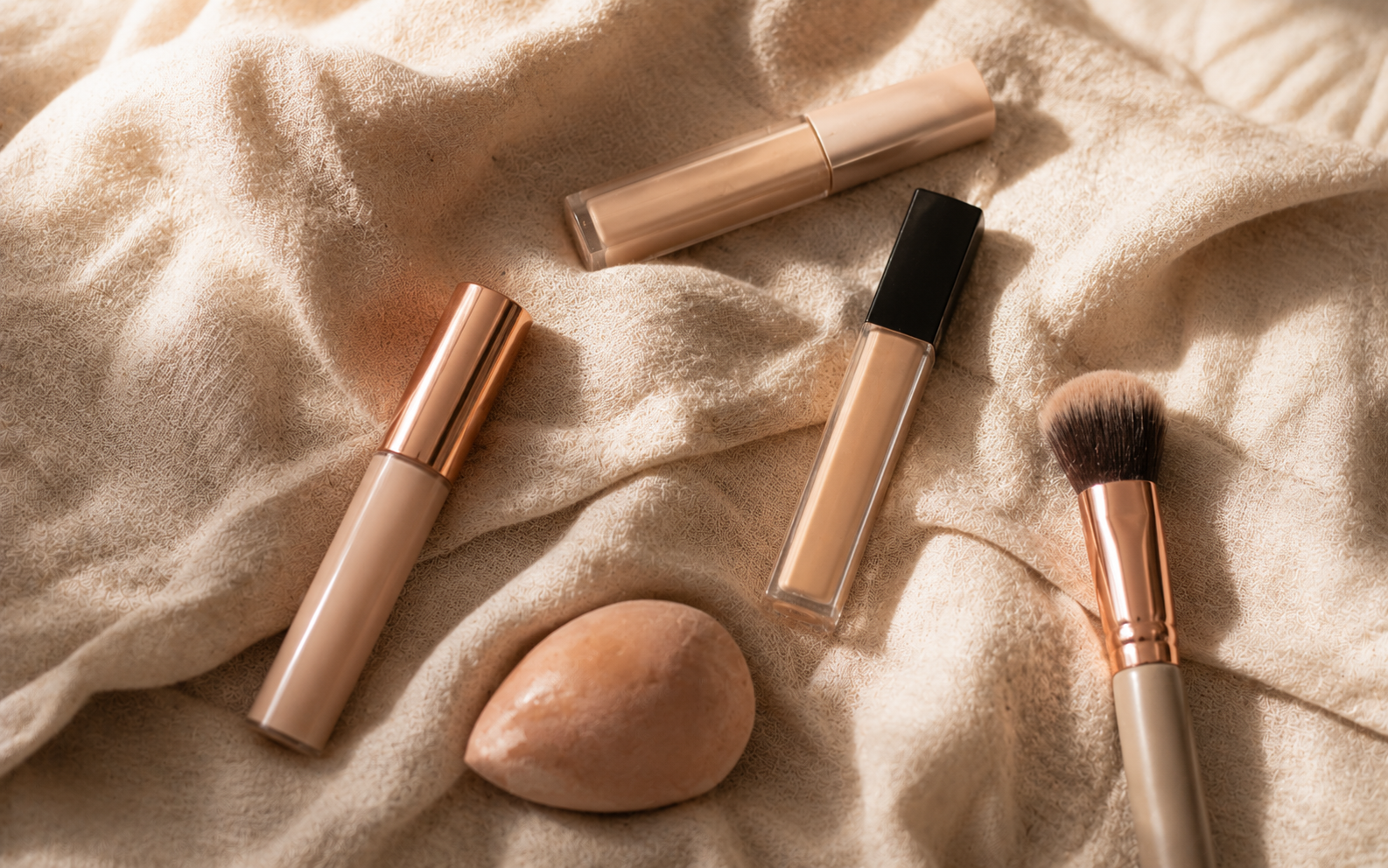 A few concealer tubes resting beside small makeup brushes and a damp blending sponge