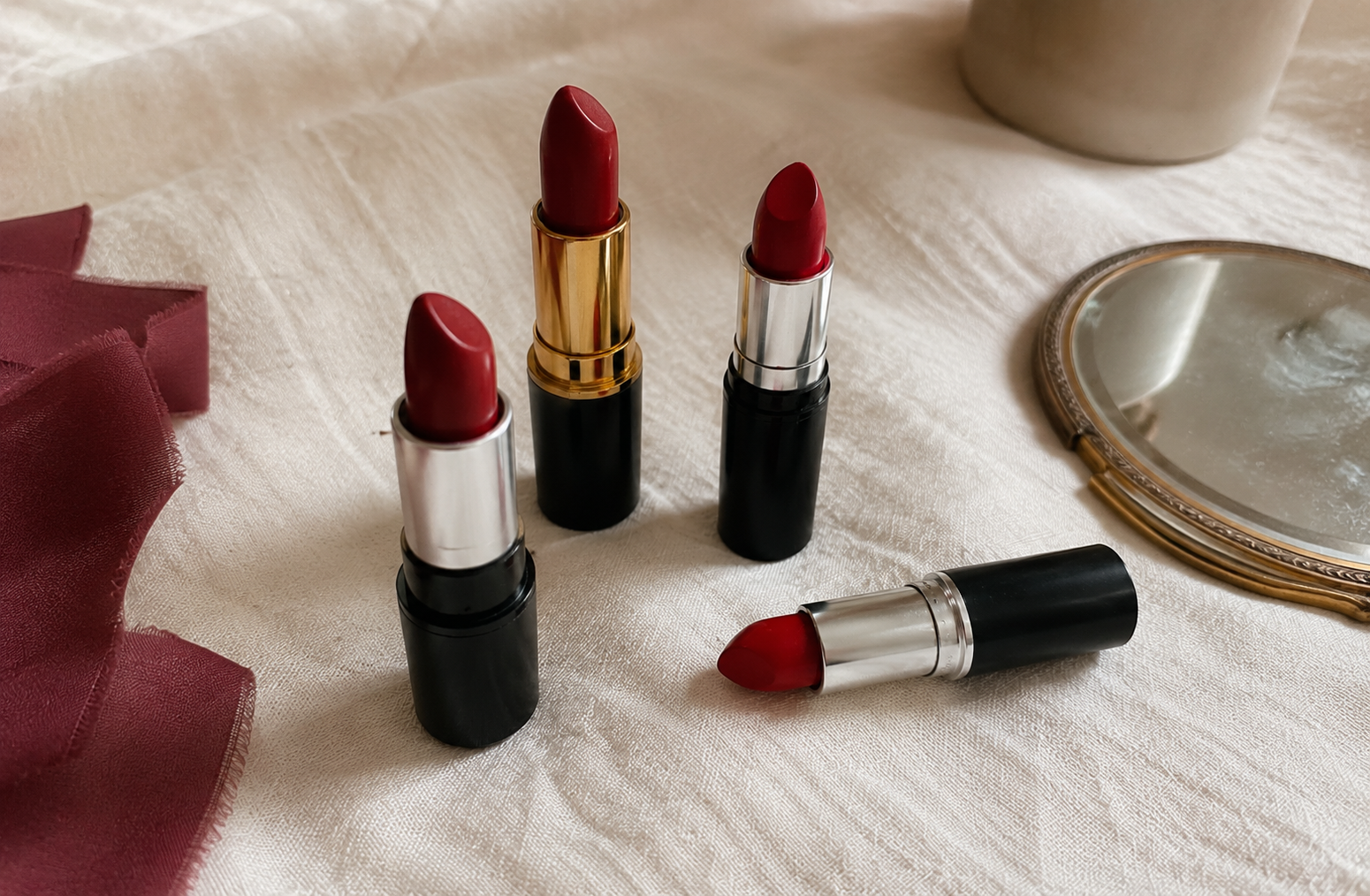 A few red lipstick tubes in different shades resting on soft ivory linen in gentle natural light