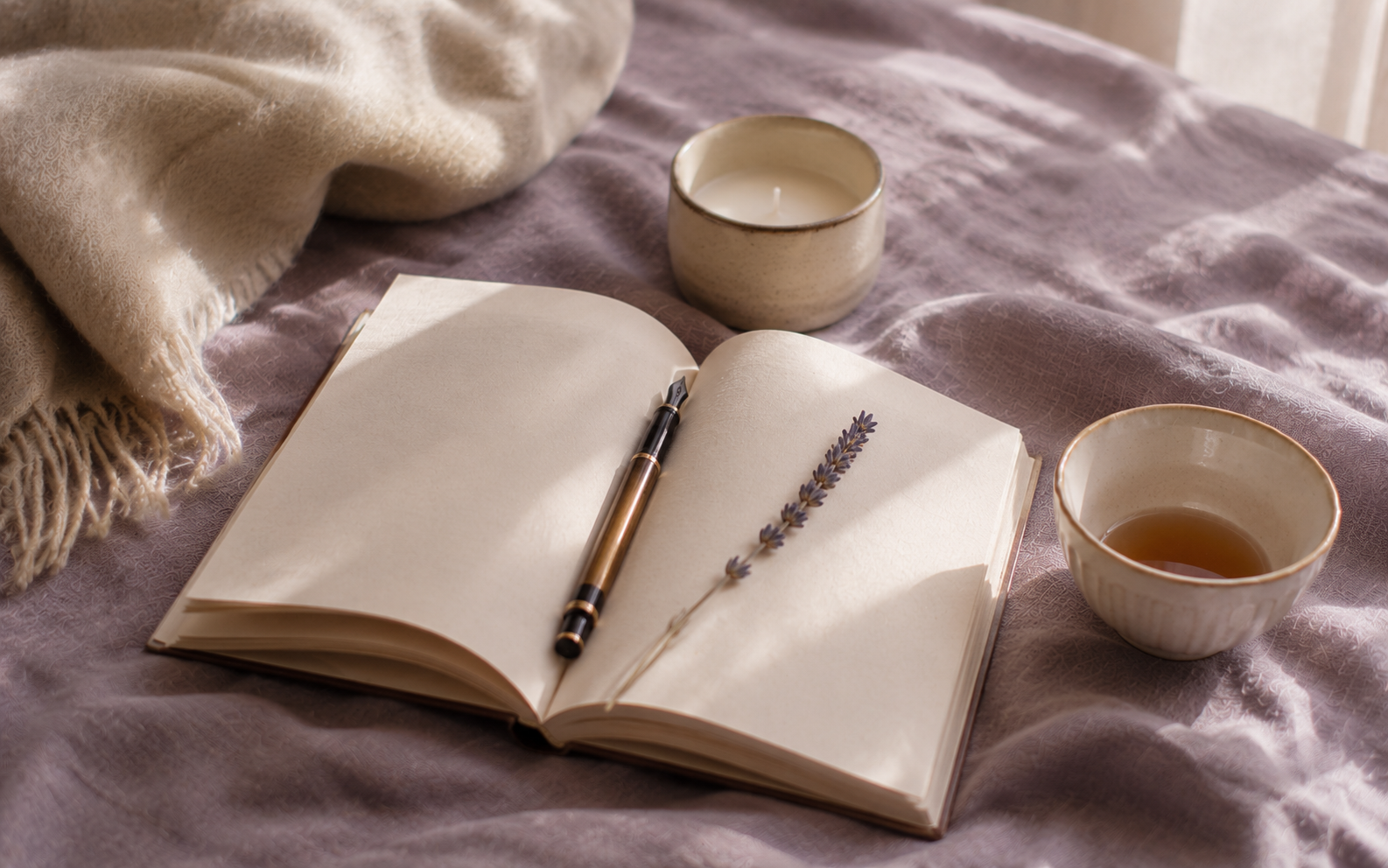An open journal and an unlit candle beside a sprig of dried lavender, the morning quietly settling in