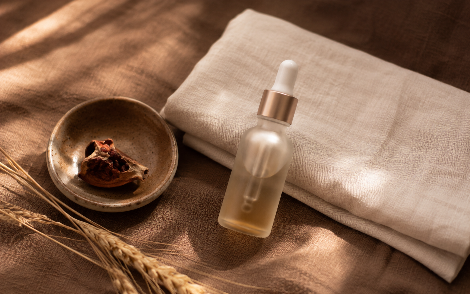 A small glass dropper bottle of brightening serum and folded cream linen catching soft natural light